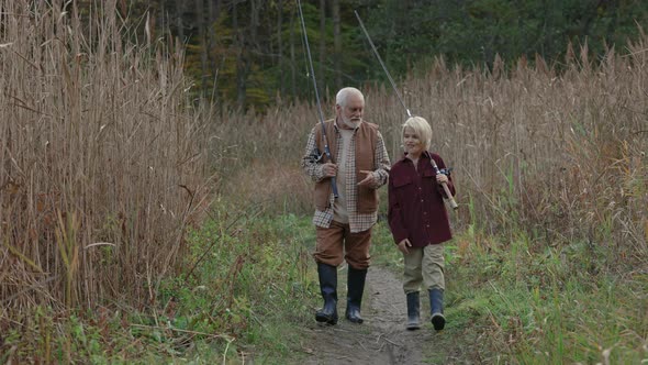 Grandpa and Grandson Walking with Fishing Rods and Talking alt