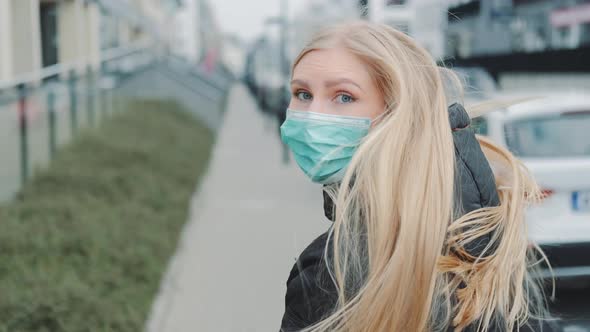 Young Blonde Woman in a Medical Mask Escaping From Somebody on the Street. alt