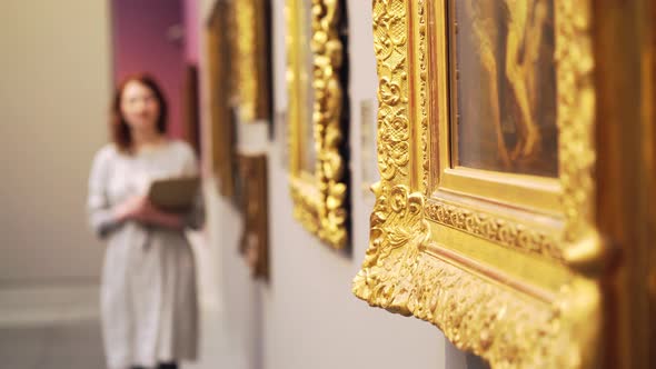 Woman Walks Along Paintings in Art Gallery