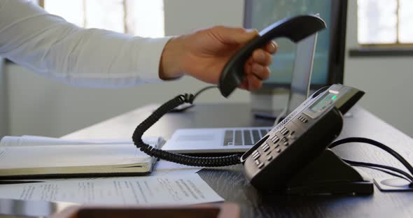 Executive putting down phone receiver at desk in office alt