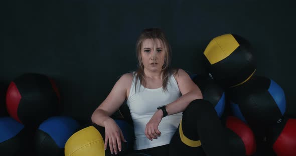 Zoom in on Beautiful Sporty Caucasian Young Woman Sitting on Gym Floor with Large Fitness Balls alt