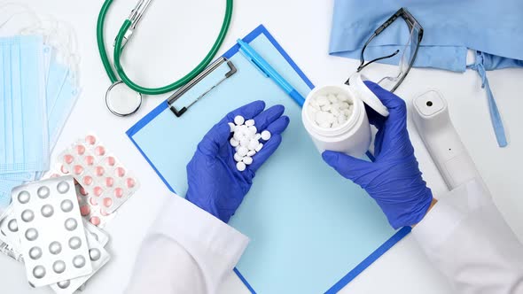 Doctor in white coat and blue latex gloves pours round white pills alt