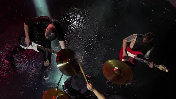 Top View of Three Rock Musicians Playing Musical Instruments in a Dark Studio in the Rain alt