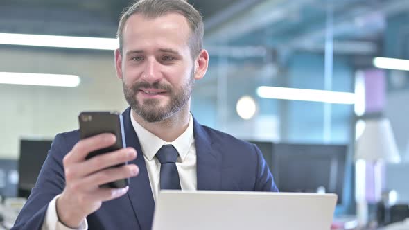 Portrait of Cheerful Businessman Using Smartphone in Office alt
