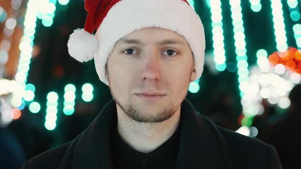 Serious Man Portrait with New Year Hat Looking at Camera, Bokeh of Christmas Garland Lights alt