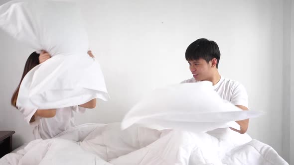 Joyful Young couple playing pillows fight on bed alt