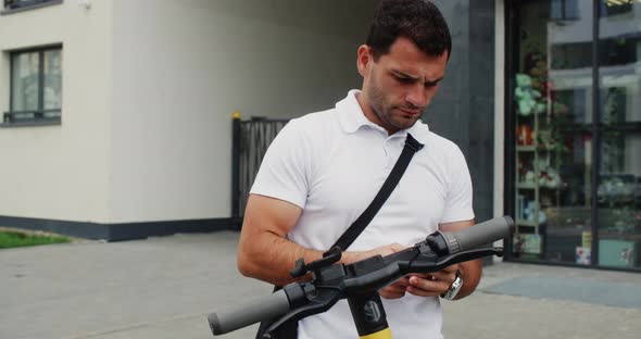 Focused Man Using Smartphone and Standing Near Escooter on Street alt