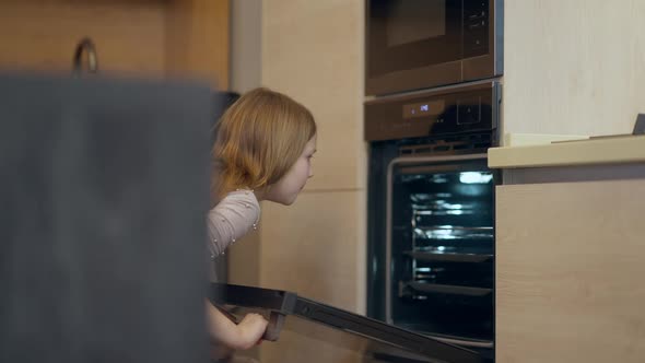 Joyful Caucasian Little Girl Looking Inside Open Oven with Mother in Household Appliances Store alt
