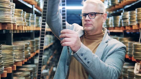 Male Employee is Looking Closely at the Old Film Tape alt