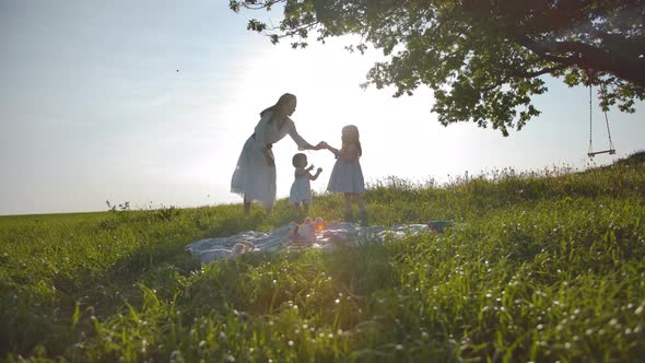 Happy Family of Mom and Two Little Daughters Are Resting in a Meadow, Far From the City. alt