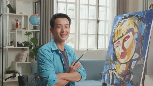 Asian Artist Man In Wheelchair Holding Paintbrush, Cross His Arms And Smile alt