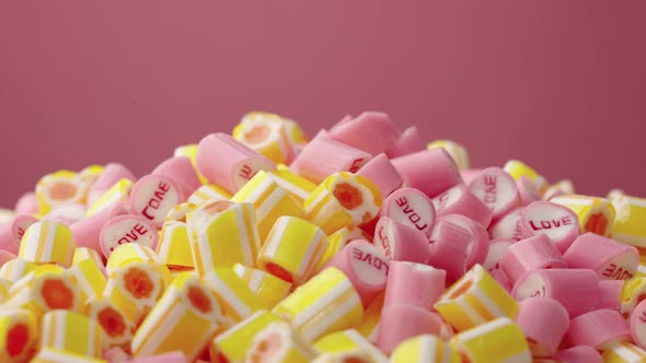 Colored Striped Caramel Candies with the Inscription Love Rotating on a Pink Background alt