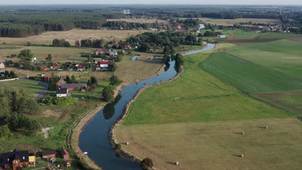 Aerial countryside shot of a farming village by the river among farms and fields and forests. alt