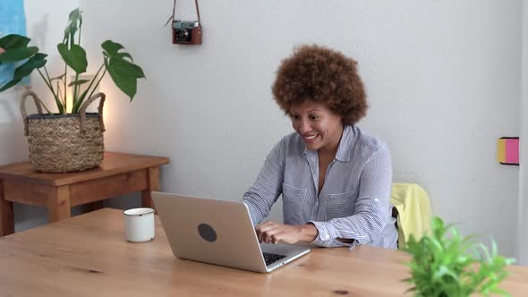 Mature african woman using laptop computer and celebrating success at home
