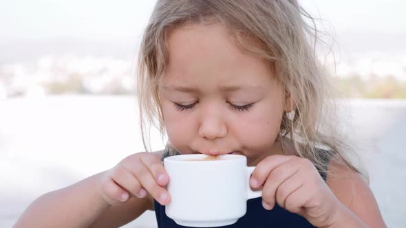 Little Blonde Girl is Drinking Cocoa From the White Cup