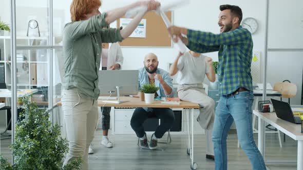 Playful Men Office Workers Fighting Paper Swords Enjoying Funny Activity Relaxing at Work alt