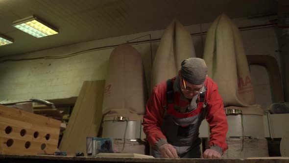 Carpenter Stands Behind the Workplace Polishes with Sandpaper Processes Wood