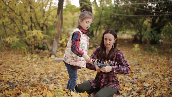Little Girl Helps Mom Clean Yellow Leaves in the Yard with a Rake