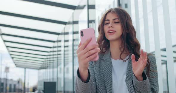 Young Successful Woman Having Video Conversation and Smiling Near Modern Building. Attractive alt