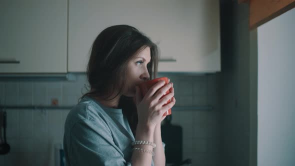 Young Relaxed Girl Look in Window and Drinks Coffee in Kitchen at Morning