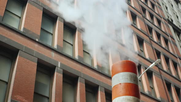 Steam Comes From the Striped Pipe, Against the Background of Tall Brick Buildings alt