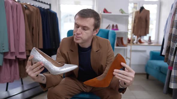 Medium Shot Portrait of Unsure Caucasian Gay Man Choosing Silver and Dark Amber Highheels Sitting in alt