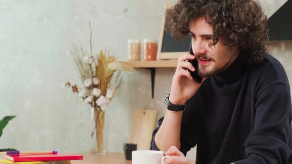 Man on Kitchen is Smiling Drinking Coffee and Talking on a Smart Phone alt