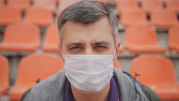 Portrait of a Sad Middleaged Man Sitting in the Stands of an Empty Stadium in a Protective Medical