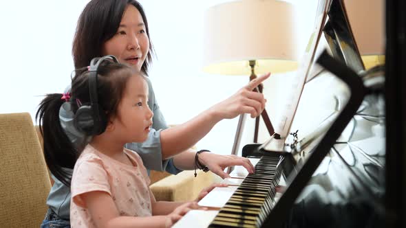 Asian mother and daughter practice piano together with happiness music class.