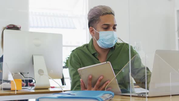 Man wearing face mask using laptop and digital tablet at office alt