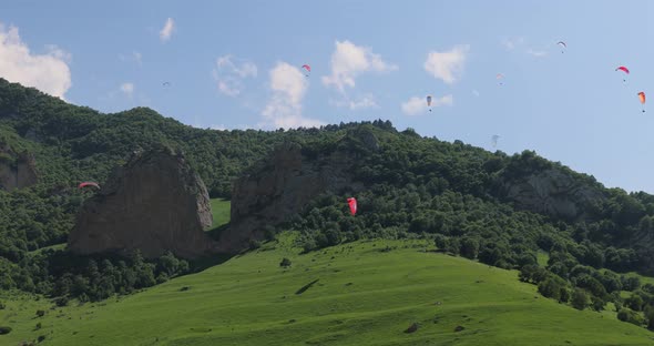 Paragliding Pilots Fly Paragliders Among Clouds and Green Mountains alt