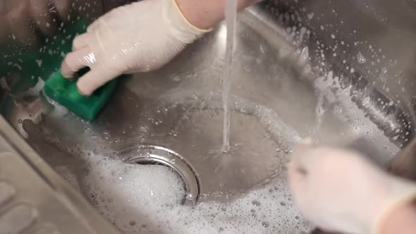 Cleaning kitchen sink with green sponge and foamed detergent alt