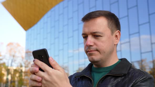 Millennial Man Stand in City Street Uses Phone and Tapping at Sunny Day