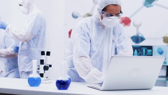 Female Scientist Stand Up and Typing on Computer in a Modern Chemistry Laboratory Dressed Up in alt