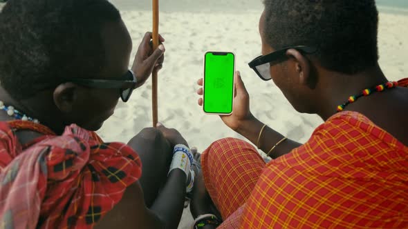 Masai Tribe Men Looking at the Smartphone and Touching Green Screen in the Front of Desert alt