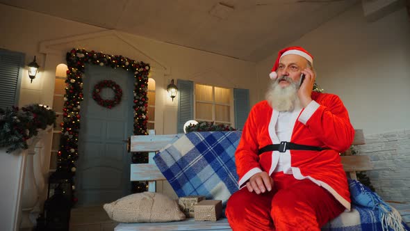 Cheerful Father Christmas Congratulating on Holiday By Smartphone.