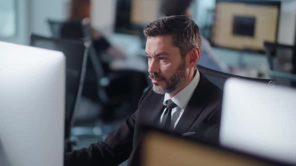 Serious Adult Bearded Man Working on Decktop Computer While Working in Big Open Space Office alt