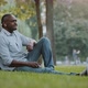 Happy Elderly African Black Businessman Wearing Wireless Headphones Sitting on Grass in City Park - VideoHive Item for Sale