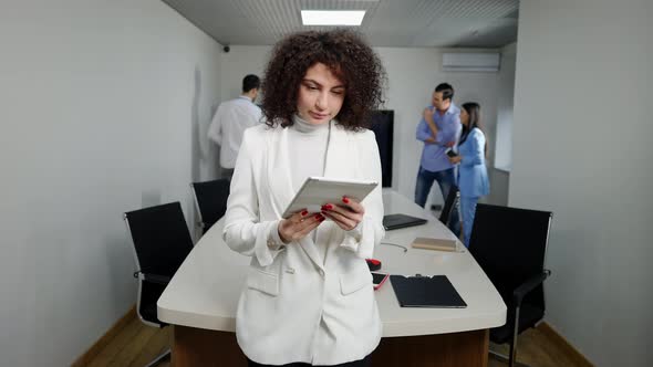 Confident Millennial Caucasian Female CEO Messaging Online on Tablet Looking at Camera and Smiling alt