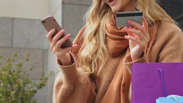 Happy Girl Customer Online Shopping Young Woman Holding Credit Card and Smartphone Sitting Outdoors alt
