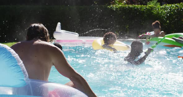 Diverse group of friends having fun playing with water guns on inflatables in swimming pool alt