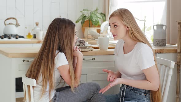 Serious Mother Blonde Caucasian Woman with Long Hair Sits on Chair in Modern Kitchen with Daughter alt