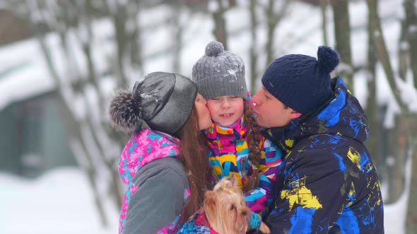 Careful Parents Kiss Girl with Small Dog in Snowy Forest alt