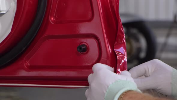 Man Is Putting Protective Vinyl Tape on Edge of Door of Car and Warming By Fan alt