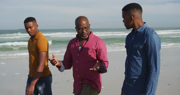 African american senior father and twin teenage sons walking on a beach and talking alt