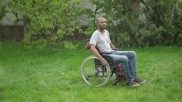 Side View Wide Shot of Confident African American Impaired Man Riding Wheelchair in Summer Garden alt
