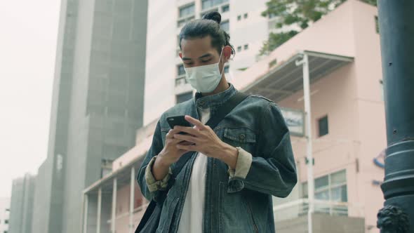 Young Asian man hipster using smartphone while standing on the street in the city.