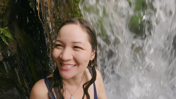 A Beautiful Asian Girl Enthusiastically Looks and Smiles Looking at a Beautiful Tropical Waterfall