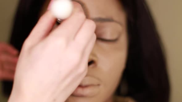 A female makeup artist applying gold makeup to a black African-American model. alt