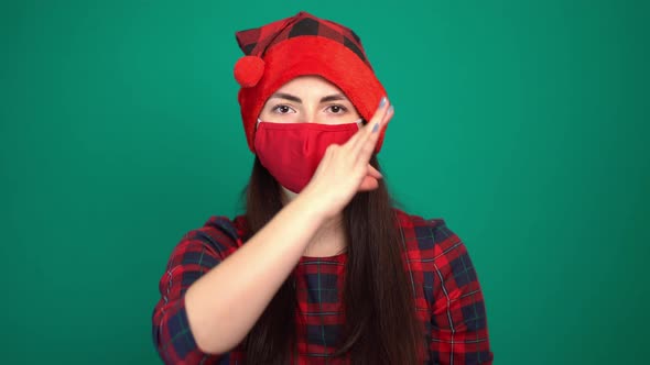 Portrait of Pretty Woman Wearing Christmas Red Hat and Medical Protective Face Mask Showing Zip